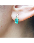 A closer front view of a yellow gold emerald earring emerald-cut with accent diamonds on top, on an woman's ear