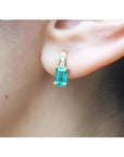 Emerald cut emerald earring in 14K yellow gold with small diamonds, worn on an ear.