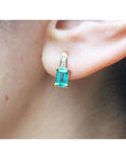 Emerald cut emerald earring in 14K yellow gold with small diamonds, worn on an ear.
