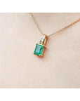Emerald pendant with diamonds on a 14K yellow gold chain, worn on a person's neck.