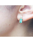 Emerald cut emerald earring in 14K yellow gold on an earlobe.