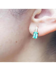 Emerald cut emerald earring in 14K yellow gold on an earlobe.