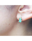 Emerald cut emerald earring in 14K yellow gold on an earlobe.