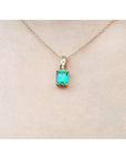 A 14k yellow gold necklace with an emerald pendant on a skin background
