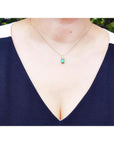 Emerald pendant on a delicate 14K yellow gold chain, worn by a person in a black and white top.