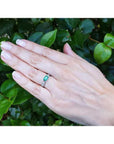 East-west emerald cut Colombian emerald ring in 14k white gold with diamond accents on a hand.