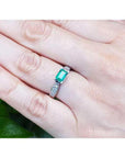 0.90 ct. East West emerald ring in 14k white gold with diamond accents, worn on a hand.