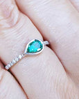A teardrop emerald bezel set ring with accent diamonds in white gold on a finger.