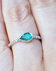 A pear cut natural colombian emerald ring with diamonds accent on a finger.