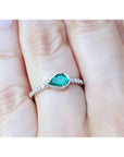 A pear cut natural colombian emerald ring with diamonds accent on a finger.
