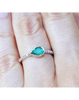A pear cut natural colombian emerald ring with diamonds accent on a finger.