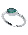 A partial side profile view of a teardrop emerald bezel set ring with accent diamonds in white gold.