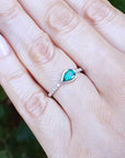 Hand wearing a ring with a bezel set natural colombian emerald against a blurred green background.