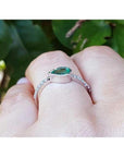 14K white gold ring with a bezel-set east-west teardrop emerald and diamond accent band.