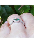 14K white gold ring with a bezel-set east-west teardrop emerald and diamond accent band.