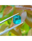 2.95 carat square natural Colombian emerald with bright medium green hue held by tweezers.