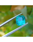 2.95 ct square natural Colombian emerald with bright medium green hue held by tweezers.