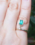 Close-up of a hand wearing emerald dangle ring May's birthstone jewelry against a blurred green background.