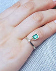 Hand wearing a gold emerald dangle ring on a purse.
