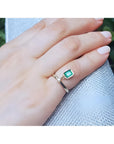 14K yellow gold ring with a bezel-set emerald dangle and small diamond accent on a finger.
