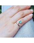 14K yellow gold ring with a bezel-set emerald dangle and small diamond accent on a finger.