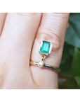 A 14k yellow gold natural colombian emerald dangle ring bezel set on a finger.