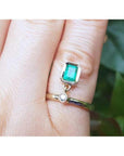 A 14k yellow gold natural colombian emerald dangle ring bezel set on a finger.