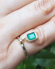 An emerald dangle ring representing May's birthstone jewelry on a hand against a blurred green background.