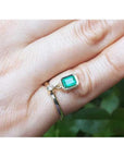 14K yellow gold ring with a bezel-set emerald dangle and small diamond accent on a finger.