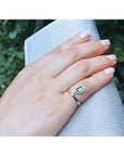 14K yellow gold ring with a bezel-set emerald dangle and small diamond accent on a hand.