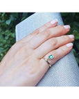 14K yellow gold ring with a bezel-set emerald dangle and small diamond accent on a hand.