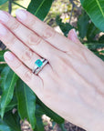 Hand wearing an emerald ring with a match band against a green leafy background.