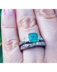 A hand wearing an emerald ring with matching wedding band made of 14k white gold.