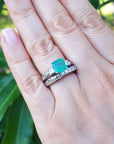 A close-up of a emerald and wedding band ring set on a green leafy background.