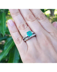1.48 ct. emerald engagement ring with diamond wedding band set in 14K white gold on a hand.