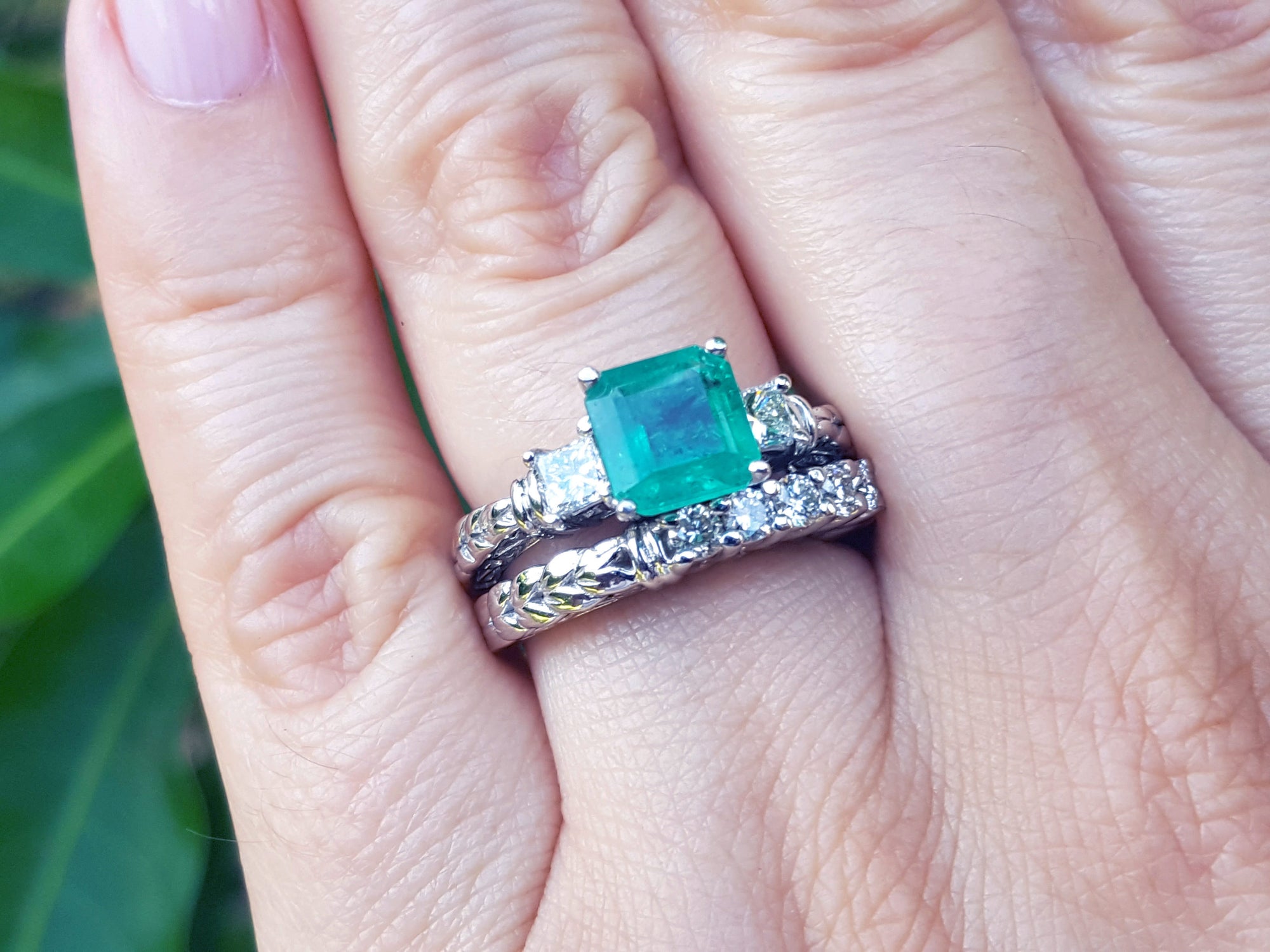 A finger wearing a macht set of emerald ring and diamond wedding band in white gold.