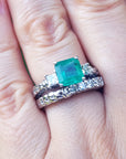 A finger wearing a macht set of emerald ring and diamond wedding band in white gold.