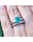 A finger wearing a macht set of emerald ring and diamond wedding band in white gold.