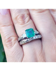 1.48 ct. emerald engagement ring and diamond wedding band set in 14K white gold on a finger.