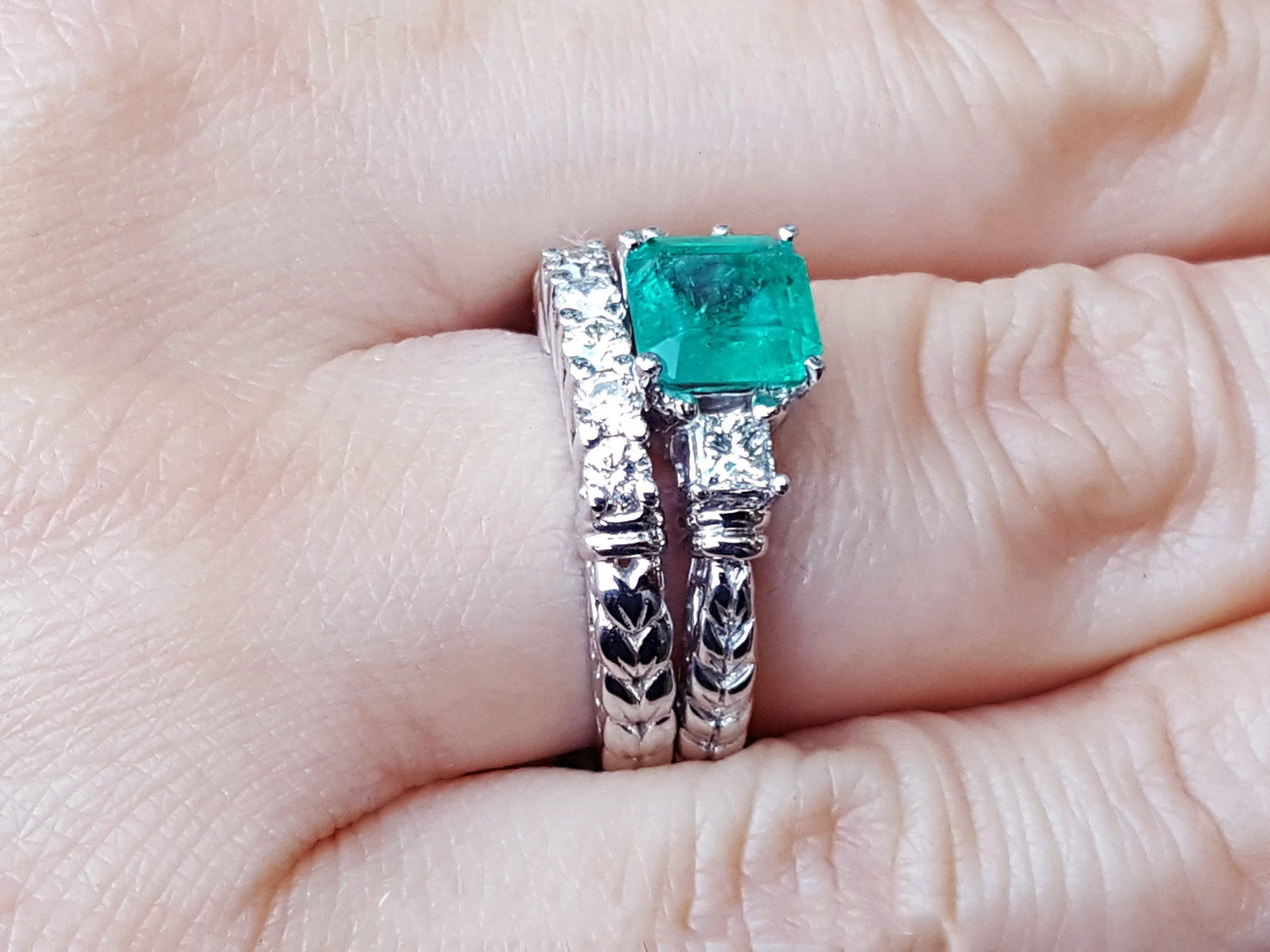 Side view of a finger wearing a matcht set emerald ring and wedding band in white gold.