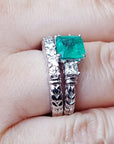 Side view of a finger wearing a matcht set emerald ring and wedding band in white gold.