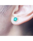 1.55 carat emerald halo diamond stud earring in 14K yellow gold on an ear.