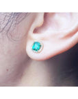 1.55 carat emerald halo diamond stud earring in 14K yellow gold on an ear.