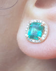 Close-up of an emerald halo diamond stud earring on a person's ear.