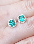 Emerald green gemstone earrings held between fingers, top view