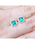 Emerald green gemstone earrings held between fingers, top view