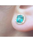 Close-up of an emerald halo diamond stud earring on a person's ear.