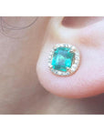 Close-up of an emerald halo diamond stud earring on a person's ear.