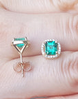 Muzo Colombian halo emerald stud earrings on a hand's fingers.
