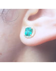 1.55 carat emerald stud earring with halo diamonds, set in 14K yellow gold, worn on an ear.